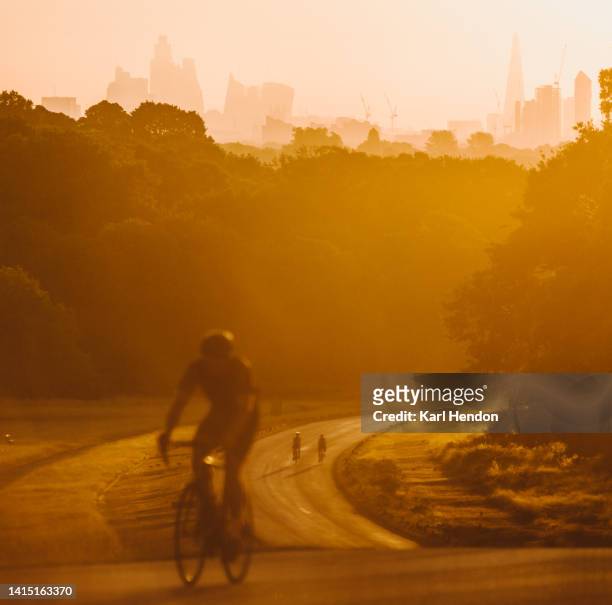 an unrecognizable cyclist on a winding road at sunrise in a london park - city of london in the background - richmond park london stock pictures, royalty-free photos & images