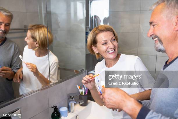 happy mature couple brushing teeth in the bathroom together - husband cleaning stock pictures, royalty-free photos & images