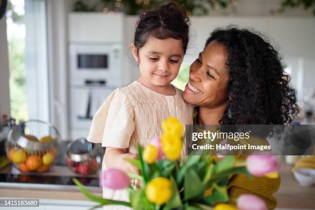 multiracial girl giving flowers her mother in their kitchen, having fun. - happy mothers day fotografías e imágenes de stock