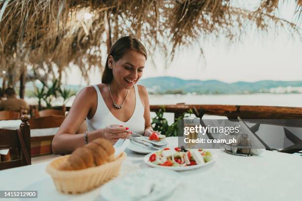 woman eating greek salad in a restaurant at the seaside in greece - griekse-gerechten stockfoto's en -beelden