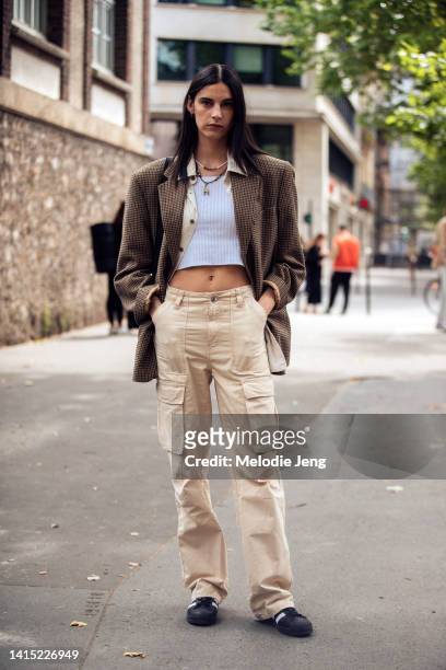 Model Cyrielle Lalande wears a boxy brown houndstooth blazer, white cropped tank top, tan cargo pants, and black and white Adidas sneakers after the...