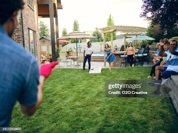 backyard party playing cornhole bean bag toss game - playing corn hole stock pictures, royalty-free photos & images