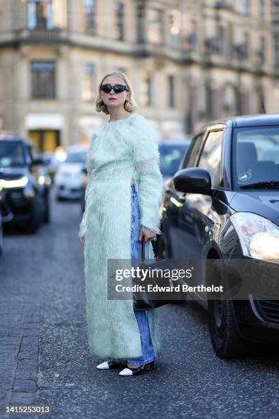 Guest wears black sunglasses, gold earrings, a pale green feather long sleeves / slit long dress, blue denim large pants, a black shiny leather Kelly...