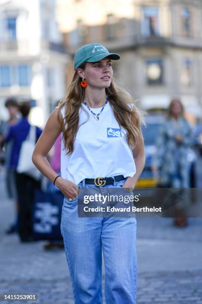 Guest wears a pale green with white embroidered pattern cap, neon orange pendant earrings, a blue and white pearls necklace, a white with blue print...