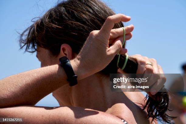 a lady tying her hair in a ponytail holding a watch in her hand and the sky in the background - woman pulling hair back stock pictures, royalty-free photos & images