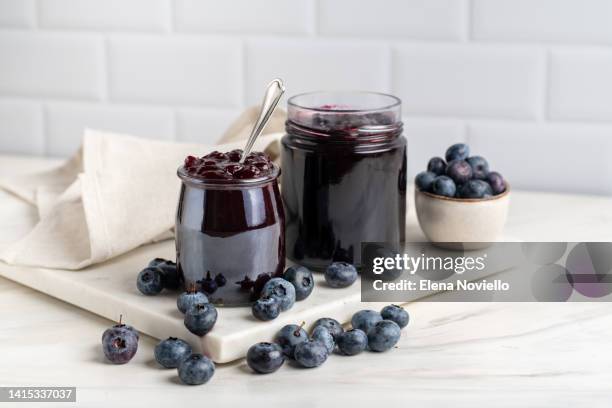 blueberry jam in a glass jar and fresh blueberries on a white marble table - blueberry stock-fotos und bilder