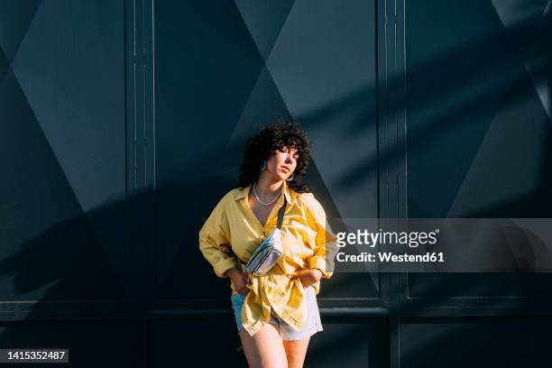 confident woman with waist pack in front of gray wall - bolsa canguro fotografías e imágenes de stock