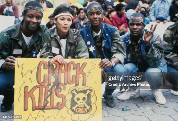 An anti-crack protestors, each wearing a headband, crouch behind a placard reading 'Crack Kills' beside a skull-and-cross bones, during an anti-crack...