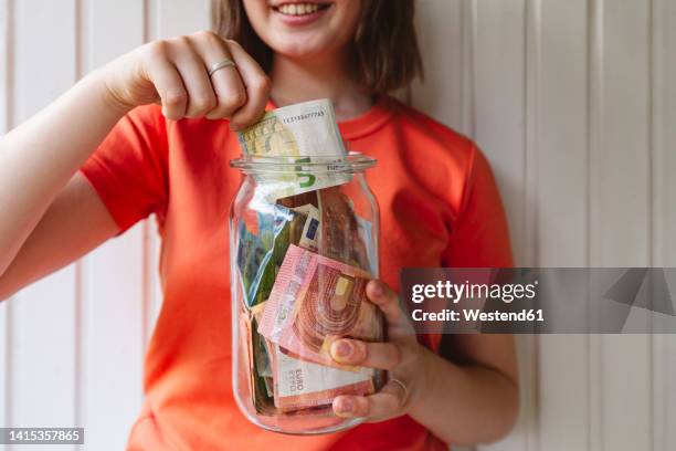 girl removing five euro banknote from glass jar - investment imagens e fotografias de stock