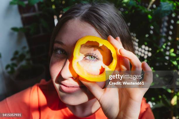 girl looking through bell pepper slice with sunlight on face - gele paprika stockfoto's en -beelden