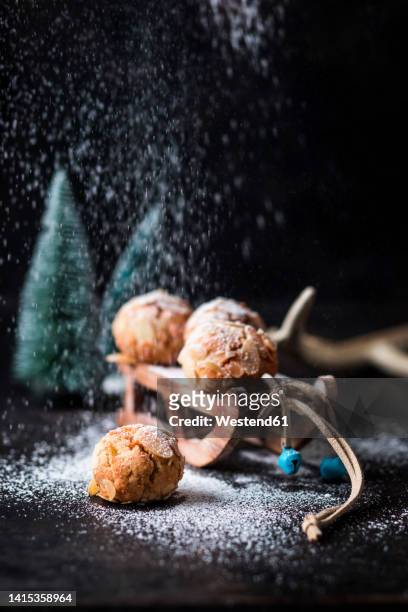 studio shot of powdered sugar pouring on miniature sled with almond cookies - powdered sugar stock-fotos und bilder