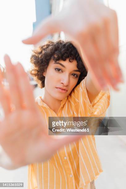 young woman with curly hair making finger frame - finger frame stock-fotos und bilder