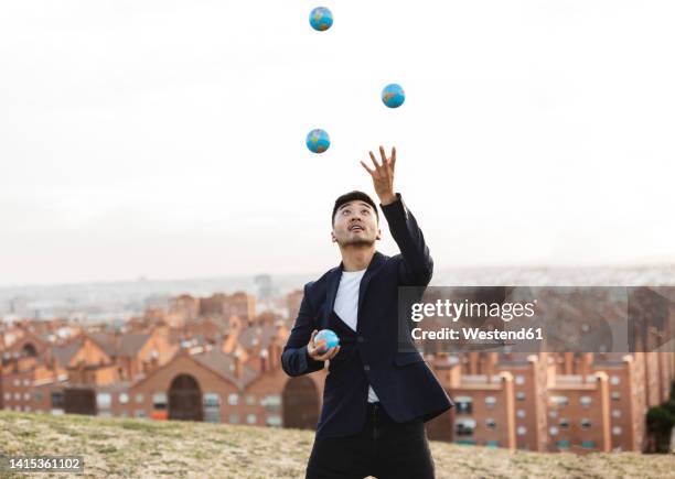 young businessman juggling globes on hill - fare il giocoliere foto e immagini stock