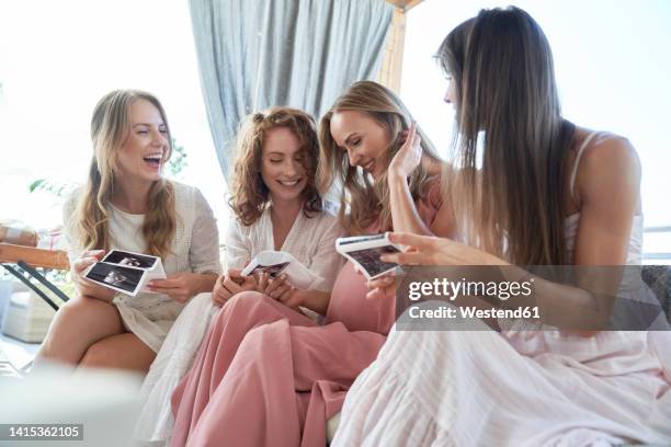 smiling pregnant woman with friends sharing her ultrasound scan result at baby shower - screening party stock-fotos und bilder