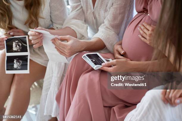 hands of pregnant woman with friends holding ultrasound scan result at baby shower - babyshower stock-fotos und bilder