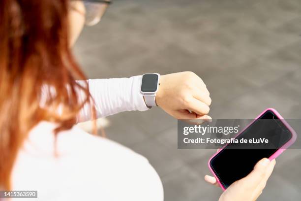 teenager wears a smartwatch and she looks at it while holding a cell phone - e girls stock pictures, royalty-free photos & images