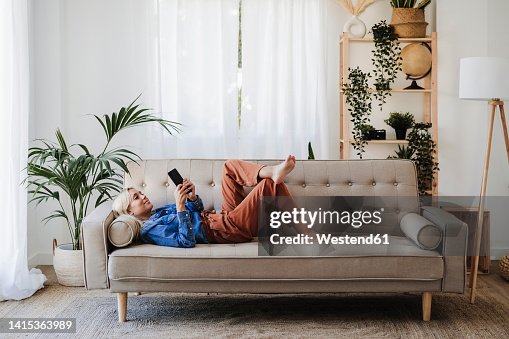 Young woman using mobile phone lying on sofa at home Young woman using mobile phone lying on sofa at home