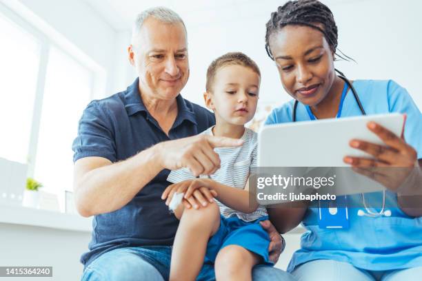 young boy sitting in the doctors office with his mature father. - family medicine stock pictures, royalty-free photos & images