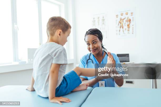 female orthopedist examining little child foot condition in clinic - podiatrist stockfoto's en -beelden