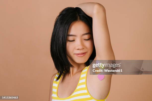 young woman with heart shape stickers on armpit against brown background - oksel stockfoto's en -beelden