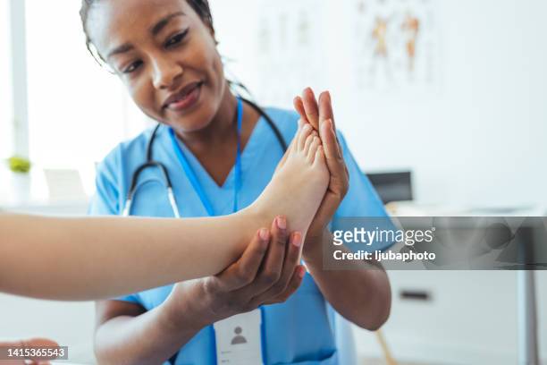 medico afro che esamina i piedi del bambino in ospedale. - caviglia foto e immagini stock