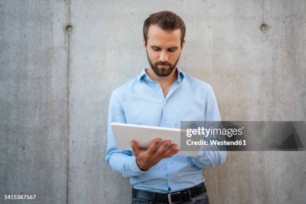 businessman using tablet pc standing in front of wall - mann vor pc stock-fotos und bilder