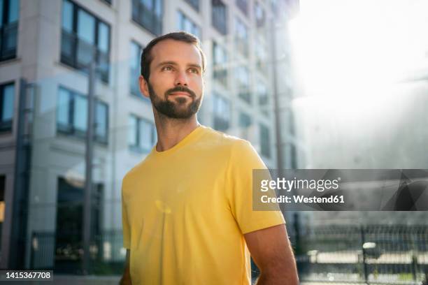 smiling young man standing in front of building on sunny day - 若い男性一人 ストックフォトと画像