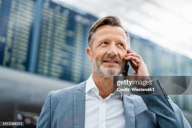 smiling mature businessman talking on smart phone - departure board front on fotografías e imágenes de stock