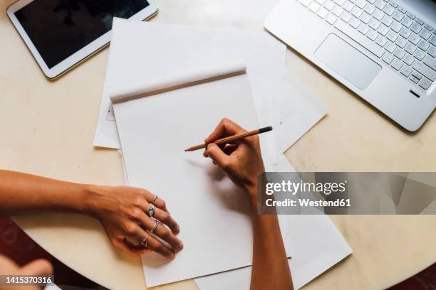 hand of fashion designer holding pencil on sketch pad at desk - schetsblok stockfoto's en -beelden