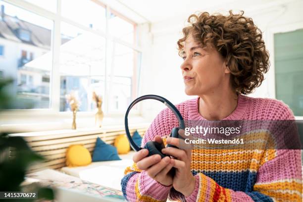 woman with brown curly hair holding wireless headphones at home - alternativer lebensstil stock-fotos und bilder