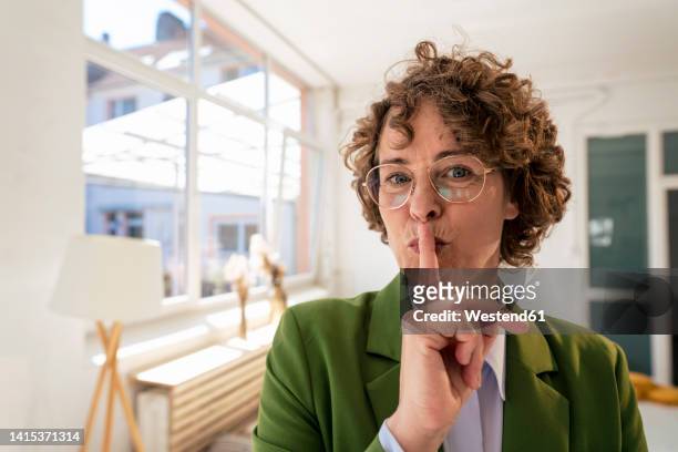 businesswoman with finger on lips in office - be silent stock-fotos und bilder