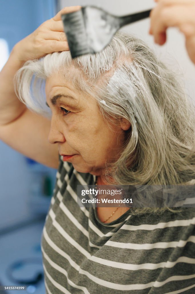 Senior woman applying dye with hairbrush at home