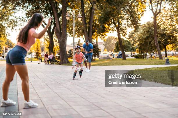 young father and mother teaching their daughter how to roller skate - roller skating in park stock pictures, royalty-free photos & images