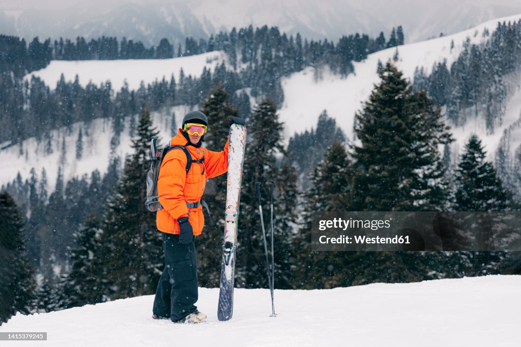 Skier with ski and poles standing in front of mountains
