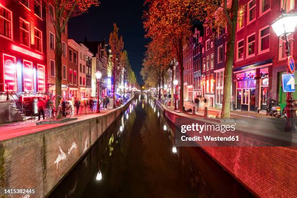 netherlands, north holland, amsterdam, long exposure of canal stretching along de wallen red light district at night - amsterdam-red-light-district-photos stockfoto's en -beelden