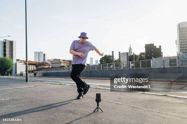 teenage boy recording dancing video on smart phone at street - young fat boys stock-fotos und bilder
