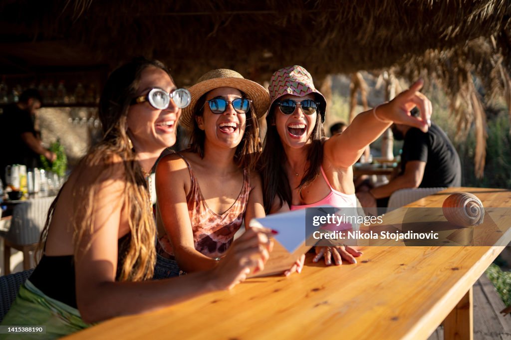 Girls having fun cheering with cocktails at bar on the beach