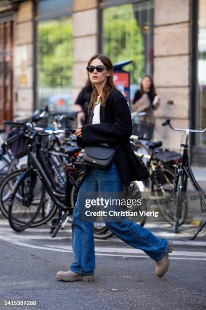 Isis-Maria Niedecken is seen wearing black Copenhagen Studios bag, grey Copenhagen Studios boots, denim jeans, black blazer on August 11, 2022 in...