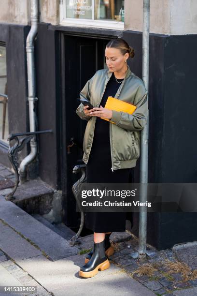 Mathilde Ravn is seen wearing yellow Copenhagen Studios bag, black brown Copenhagen Studios boots, black skirt with slit, olive bomber jacket on...