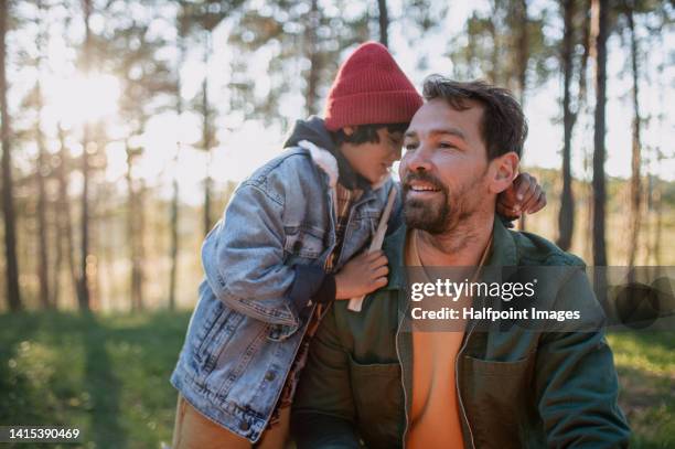 a happy small multiracial boy with father hugging when preparing wood for campfire in forest. - axe stock pictures, royalty-free photos & images