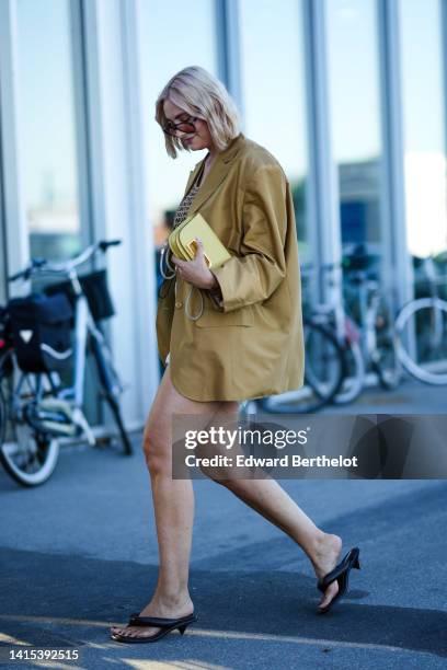 Guest wears orange sunglasses, gold pendant earrings, a brown with black inscriptions print pattern V-neck / cropped tank-top from Munthe, a beige...