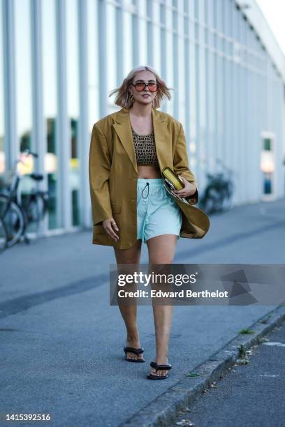 Guest wears orange sunglasses, gold pendant earrings, a brown with black inscriptions print pattern V-neck / cropped tank-top from Munthe, a beige...