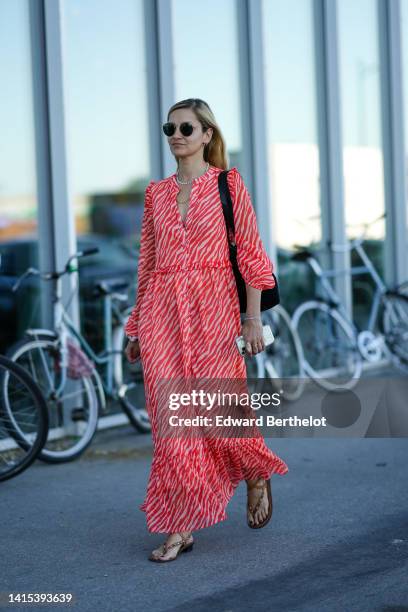 Guest wears black circle sunglasses, gold earrings, a white pearls necklace, a gold chain necklace, a red and pale red zebra print pattern long...