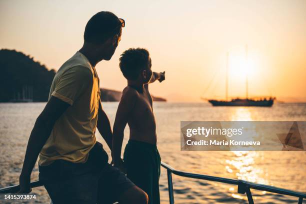 father and son looking out from boat. - father son sailing stock-fotos und bilder