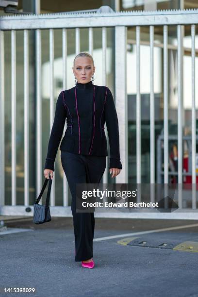 Guest wears silver pendant earrings, a black felt high neck / zipper jacket, black suit pants, a black shiny leather handbag, neon pink satin / silk...