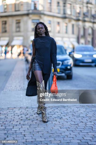 Guest wears gold earrings, a black asymmetric long sleeves / asymmetric dress, black shiny leather shorts, a neon orange shiny leather handbag, beige...