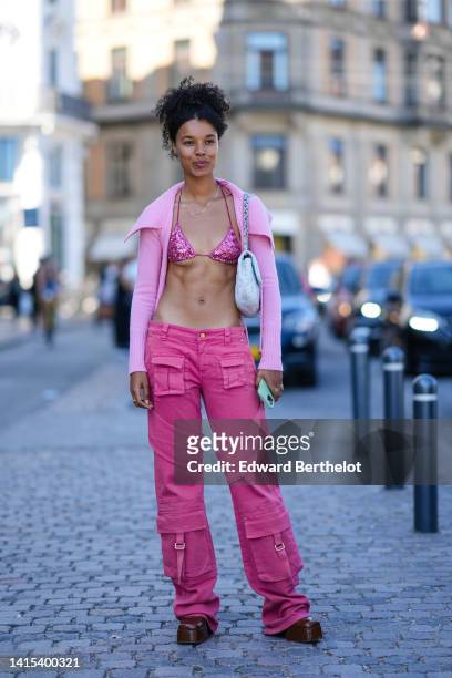 Guest wears a pale pink wool high neck / ribbed cardigan, a pink shiny sequined bra swimwear, a pale blue fluffy shoulder bag, pink wide legs cargo...