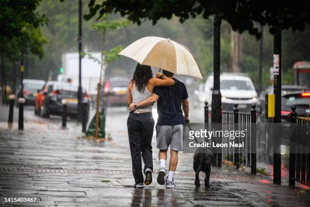 Couple shelter under an umbrella during a dog walk, as torrential rain and thunderstorms hit the country on August 17, 2022 in London, England. After...