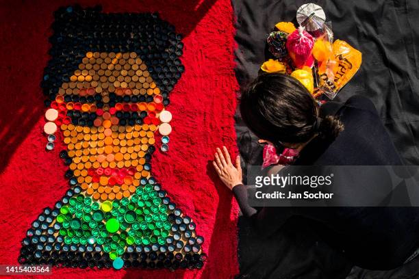 Mexican female artist, employing plastic bottle caps and dyed sawdust, creates a portrait picture of the Mexican painter Frida Kahlo during the Day...