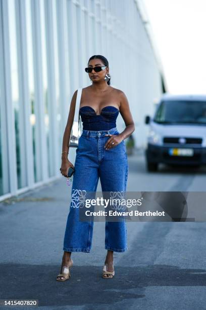 Guest wears black sunglasses from Prada, oversized silver earrings, a navy blue denim heart neck / shoulder-off body, a silver shiny varnished...